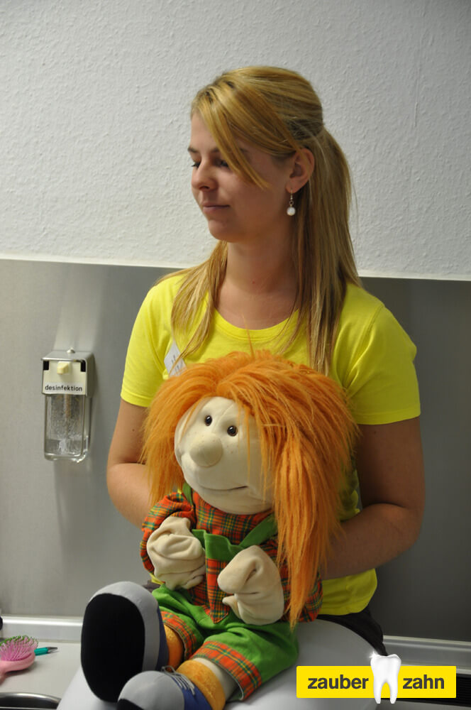 Mitarbeiterin hält eine Handpuppe mit orangefarbenen Haaren.
