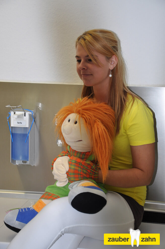 Mitarbeiterin hält eine Handpuppe mit orangefarbenen Haaren.