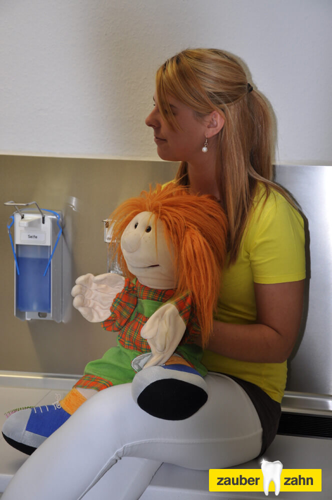 Mitarbeiterin hält eine Handpuppe mit orangefarbenen Haaren.