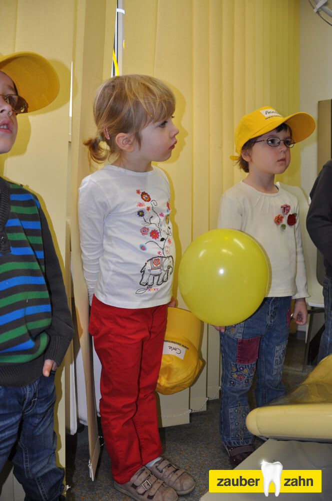 Mehrere Kinder stehen mit einem gelben Luftballon im Behandlungszimmer.
