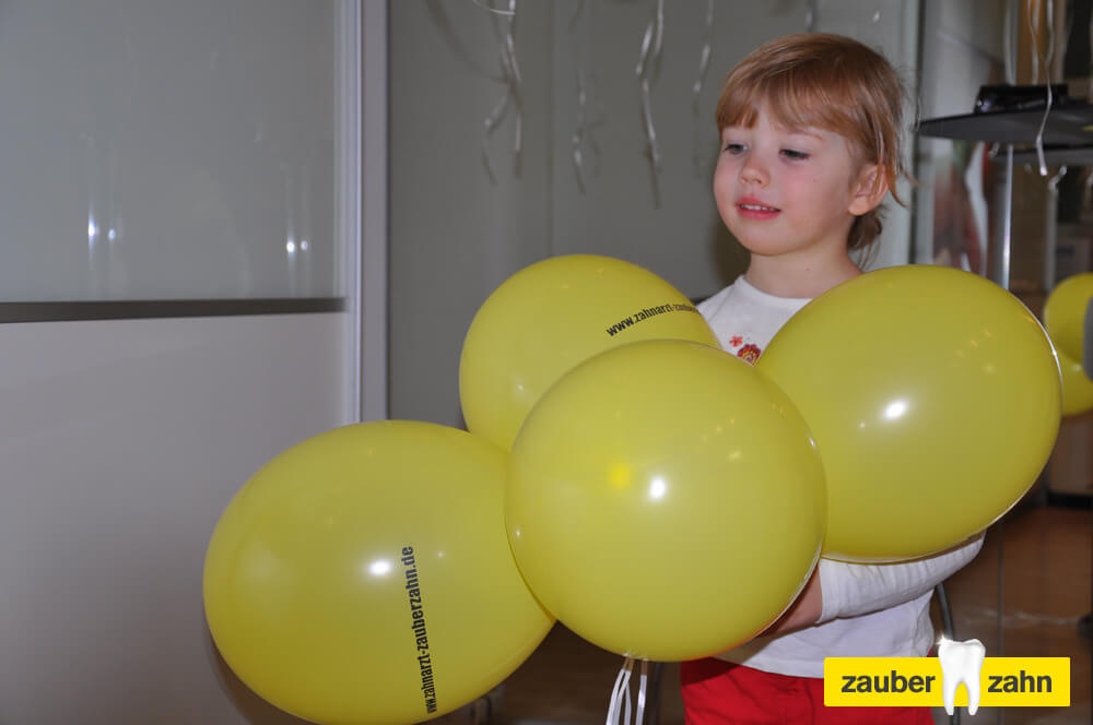 Kind steht hinter mehreren gelben Luftballons.