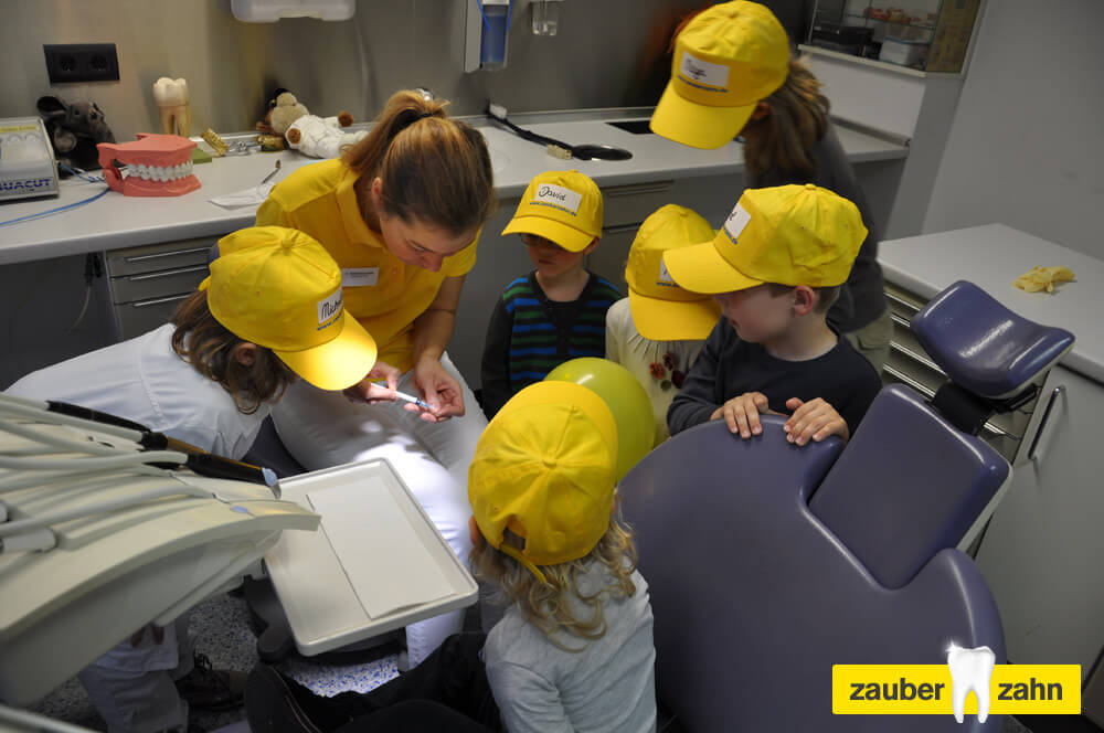 Mitarbeiterin zeigt mehreren Kindern etwas im Behandlungszimmer.