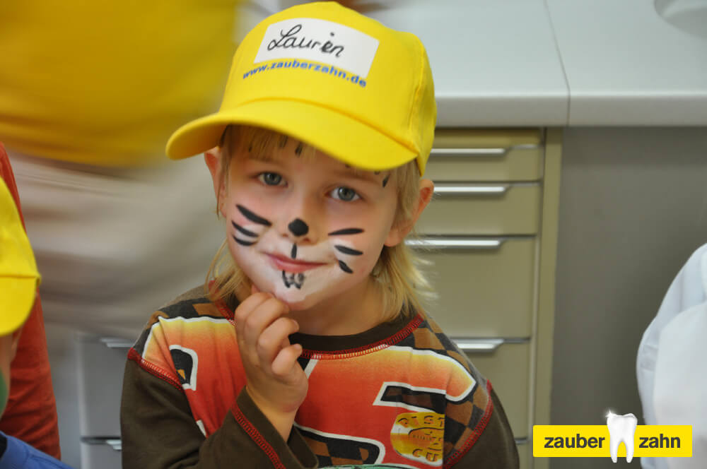 Kind mit gelber Kappe und als Katze bemaltem Gesicht.