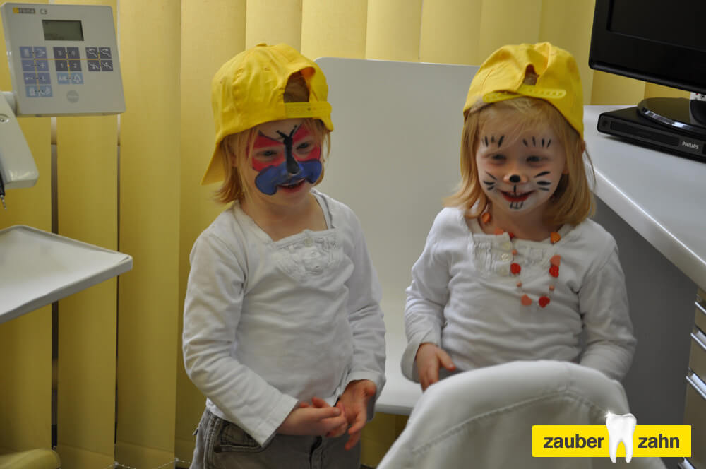 Zwei Kinder mit gelben Kappen und bunt bemalten Gesichtern stehen nebeneinander.