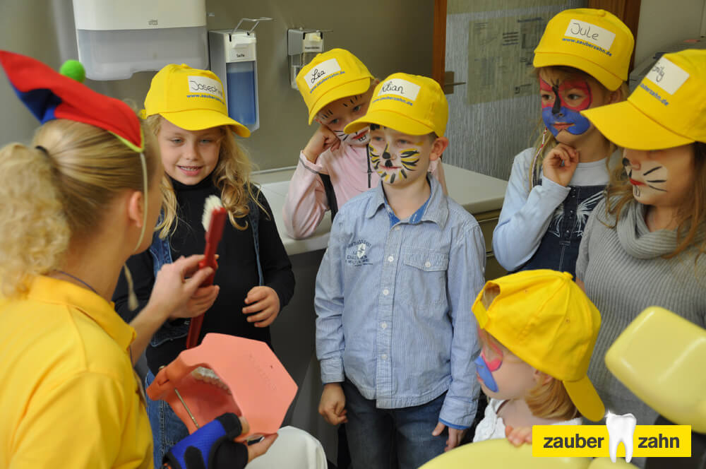 Kinder mit gelben Kappen und bemalten Gesichtern stehen gemeinsam im Behandlungszimmer.