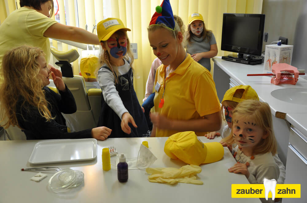 Mitarbeiterin mit bunter Kopfbedeckung steht mit Kindern an einer Ablage im Behandlungszimmer.