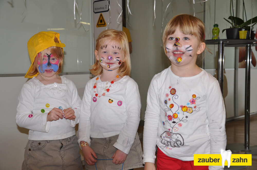 Drei Kinder mit bunt bemalten Gesichtern stehen nebeneinander.