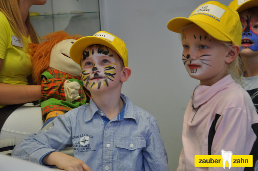 Zwei Kinder mit gelben Kappen und bemalten Gesichtern im Behandlungszimmer.