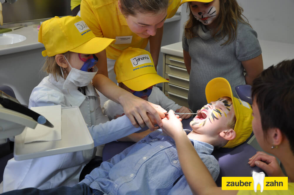 Kinder probieren gegenseitig zahnärztliche Instrumente aus, während ein Kind auf dem Behandlungsstuhl liegt.