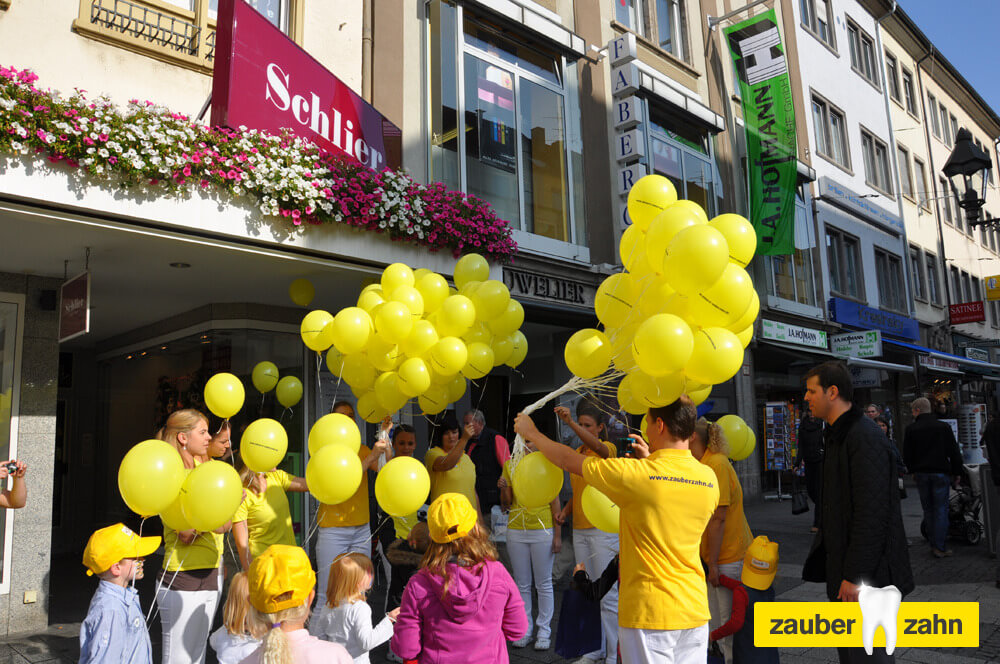 Kinder und Erwachsene mit zahlreichen gelben Luftballons in einer Fußgängerzone.