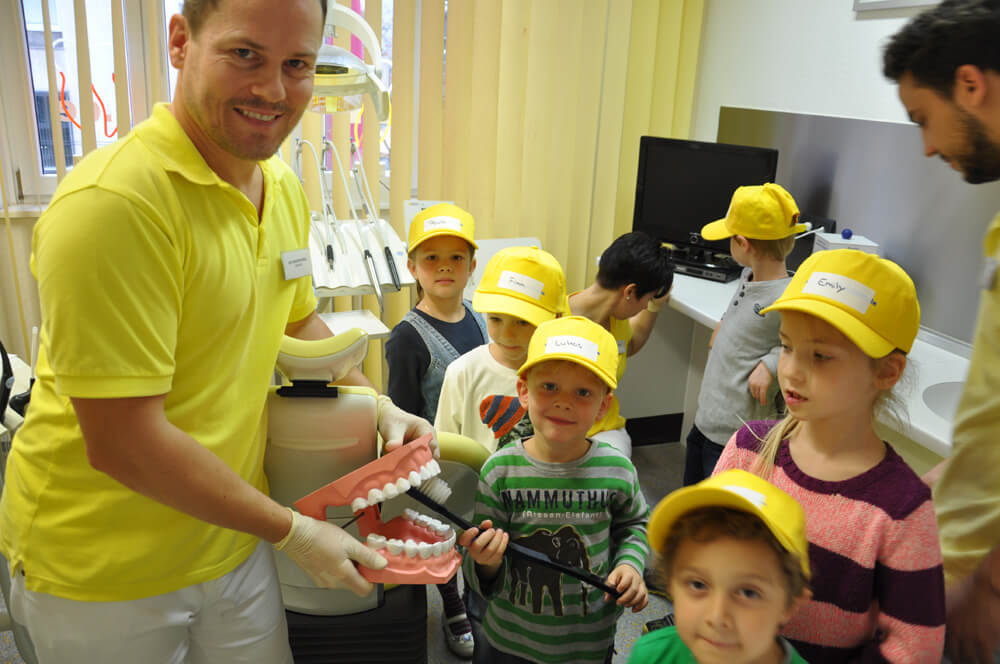 Mitarbeiter hält ein Gebissmodell vor einer Gruppe von Kindern.