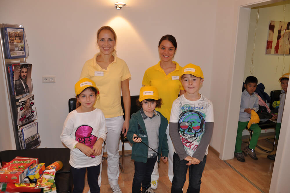 Zwei Mitarbeiterinnen und drei Kinder mit gelben Kappen posieren für ein Gruppenfoto.