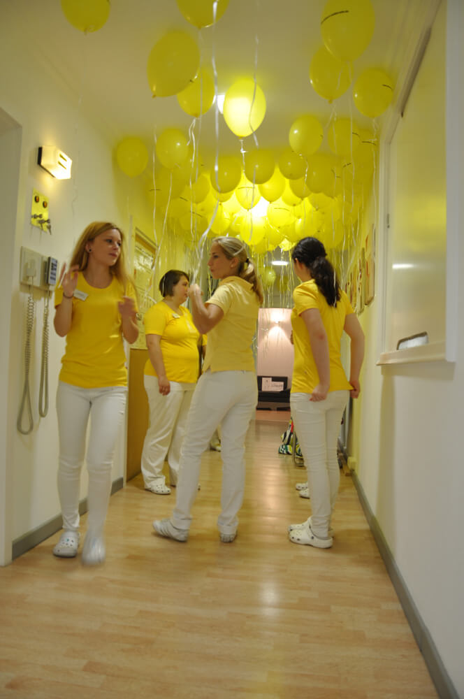 Drei Mitarbeiterinnen stehen in einem mit gelben Luftballons geschmückten Flur.