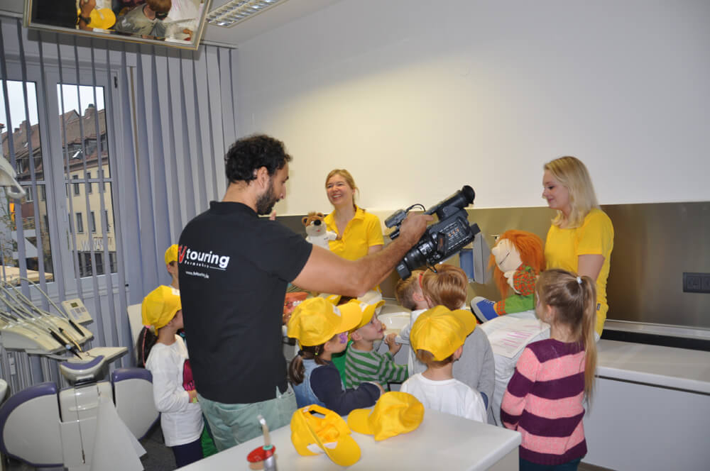 Person mit Kamera filmt Kinder und Mitarbeiterinnen in einem Raum.