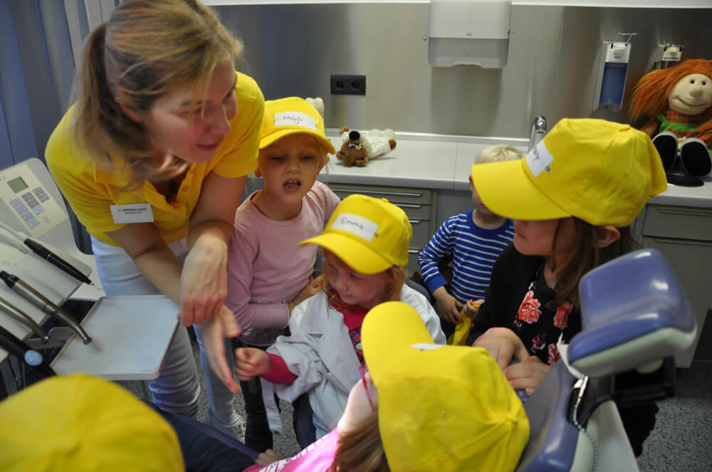 Mitarbeiterin sitzt mit mehreren Kindern mit gelben Kappen zusammen.
