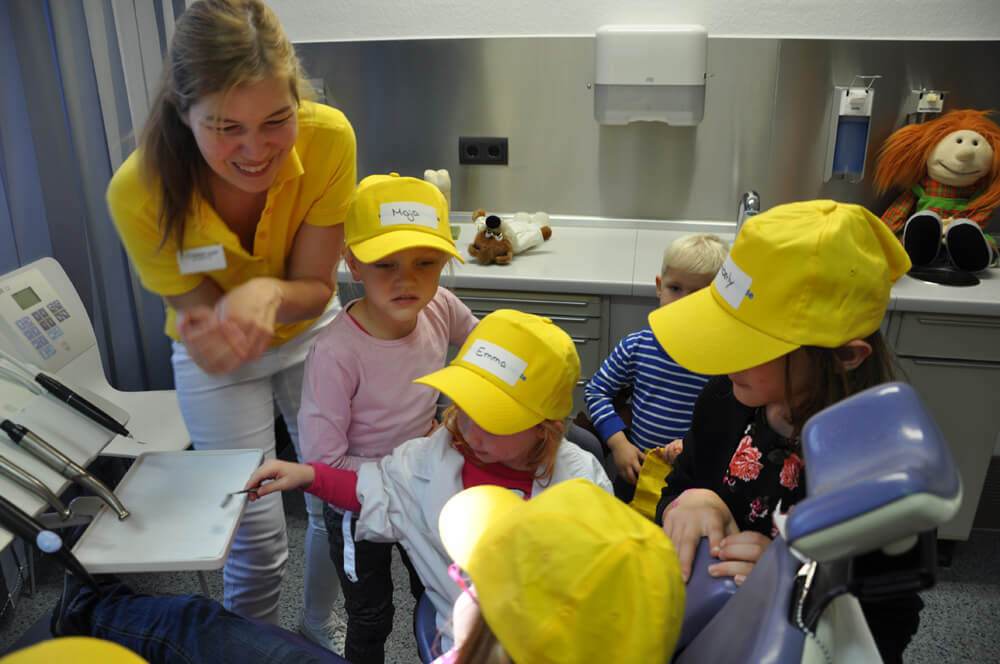 Mitarbeiterin zeigt mehreren Kindern etwas im Behandlungszimmer.