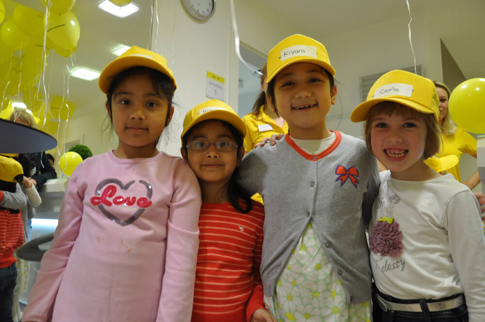 Vier Kinder mit gelben Kappen stehen gemeinsam für ein Foto.