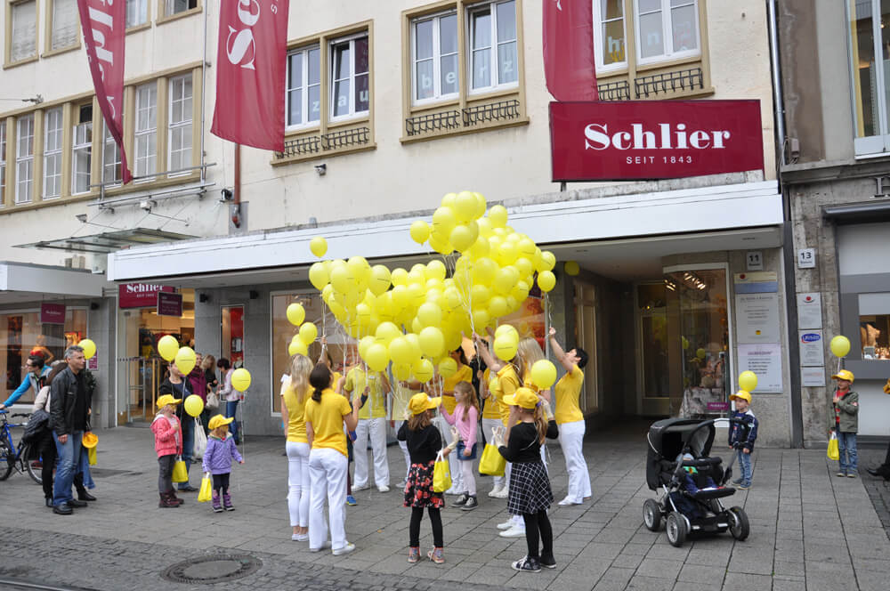 Praxisteam und weitere Personen mit gelben Luftballons vor einem Gebäude.