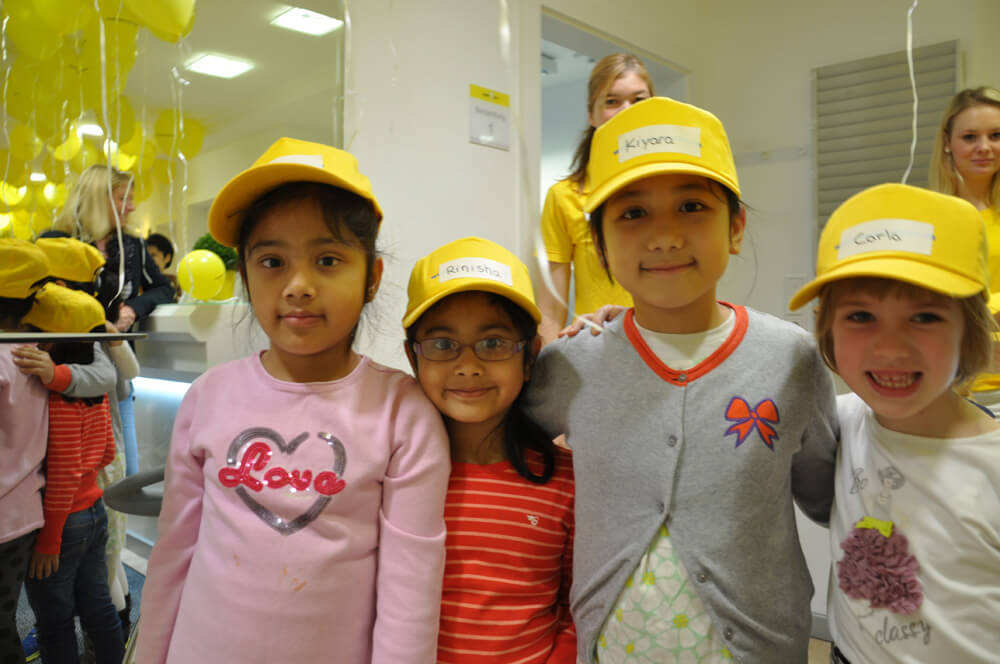 Vier Kinder mit gelben Kappen stehen nebeneinander.