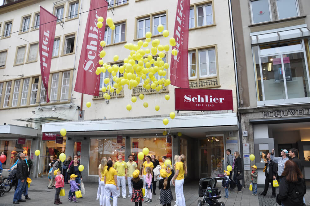 Praxisteam und weitere Personen mit gelben Luftballons vor einem Gebäude.