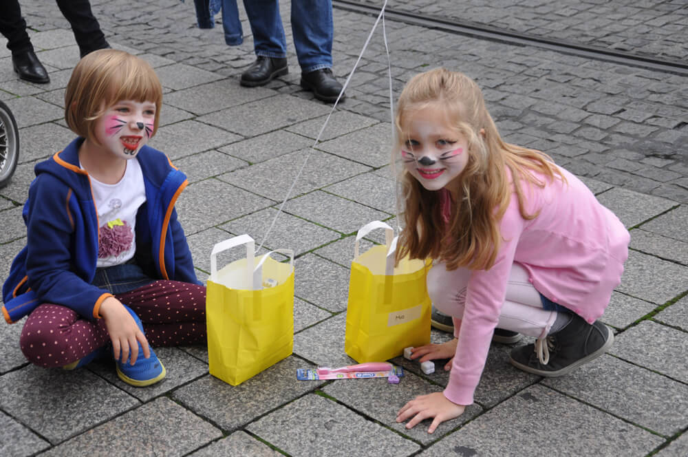 Kinder mit bemalten Gesichter sitzen auf dem Boden neben gelben Tüten.