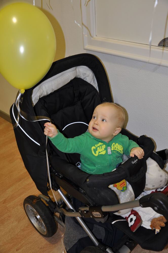 Kleinkind im Kinderwagen hält die Schnur eines gelben Luftballons.