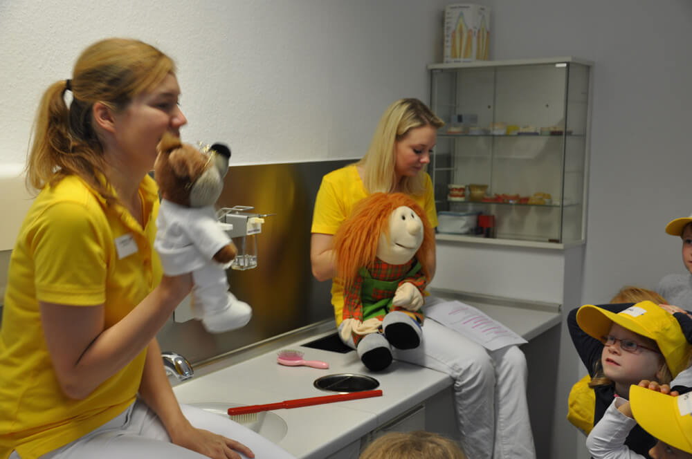 Zwei Mitarbeiterinnen sitzen mit Handpuppen im Behandlungszimmer.