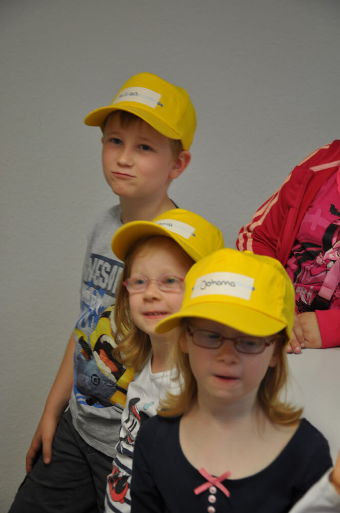 Drei Kinder mit gelben Kappen stehen nebeneinander.