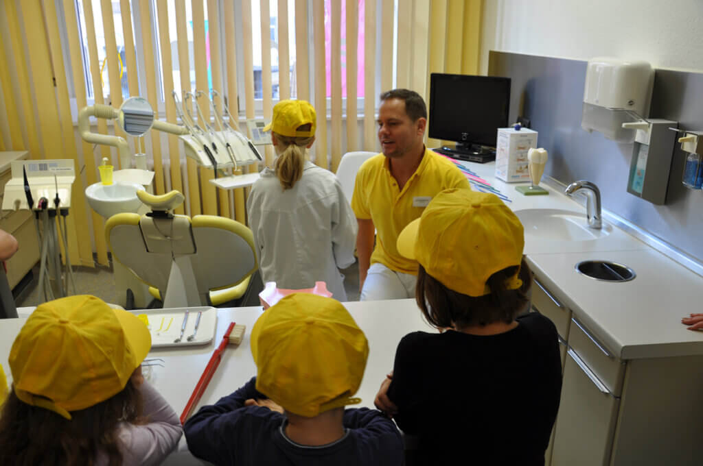 Mitarbeiter erklärt Kindern eine zahnärztliche Behandlungseinheit.