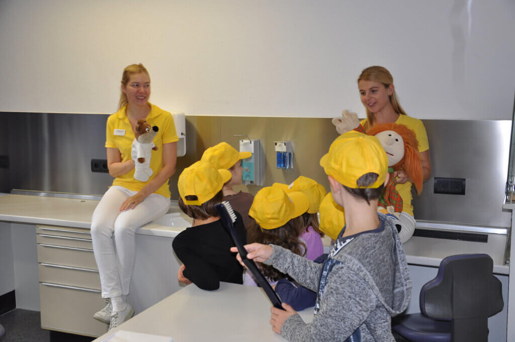 Mitarbeiterin zeigt Kindern Zähneputzen mit einer Handpuppe.