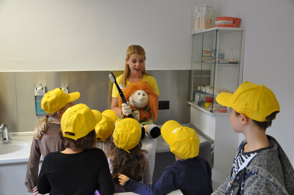 Mitarbeiterin zeigt Kindern Zähneputzen mit einer Handpuppe.