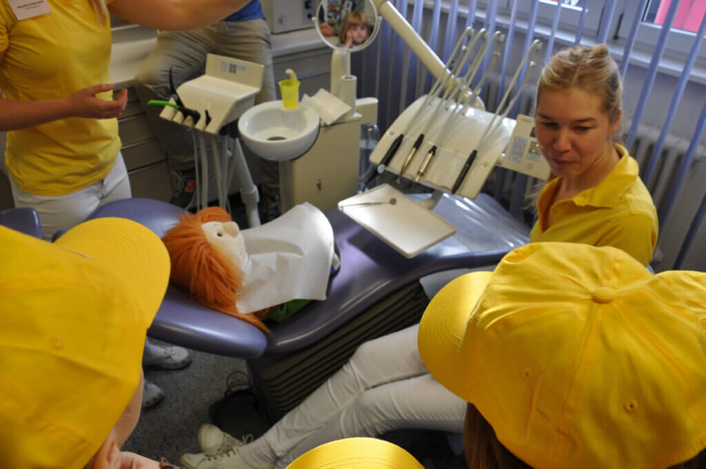 Mitarbeiterin zeigt Kindern mit einer Handpuppe eine zahnärztliche Behandlung.