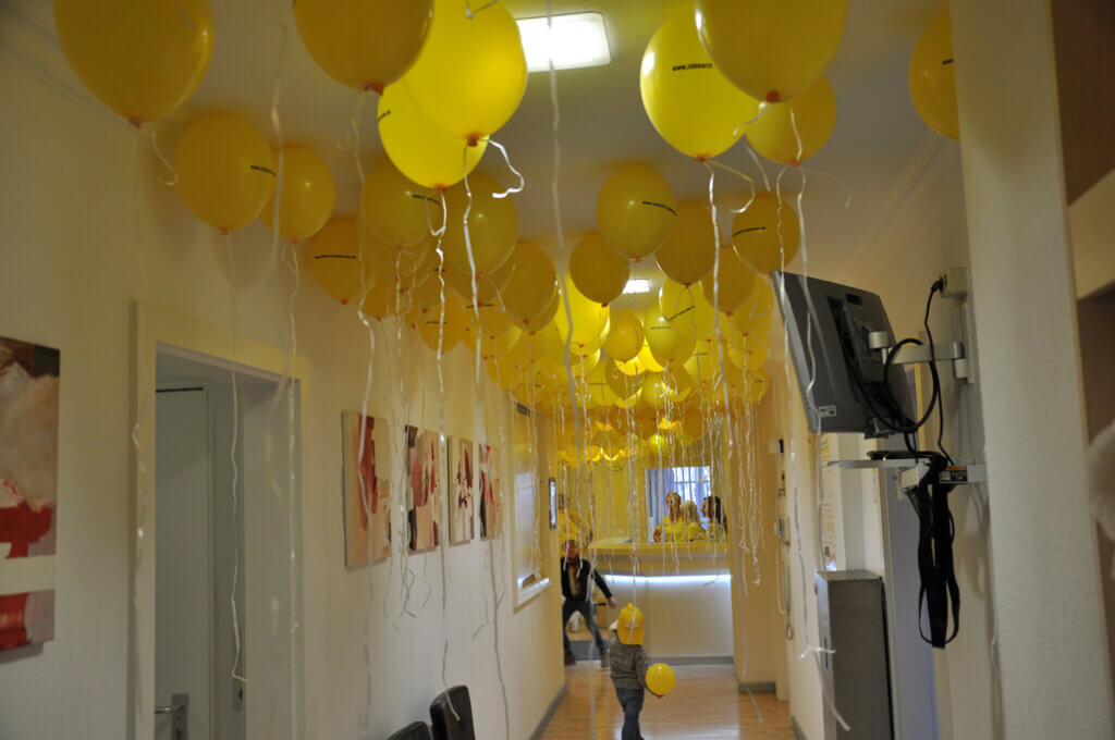 Flur der Zahnarztpraxis mit zahlreichen gelben Luftballons und einem glücklichen Kind.
