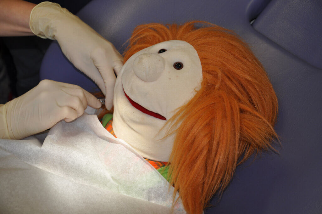 Handpuppe liegt auf einem zahnärztlichen Behandlungsstuhl.