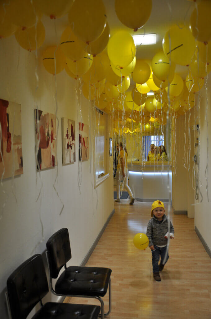 Flur der Zahnarztpraxis mit zahlreichen gelben Luftballons und einem glücklichen Kind.