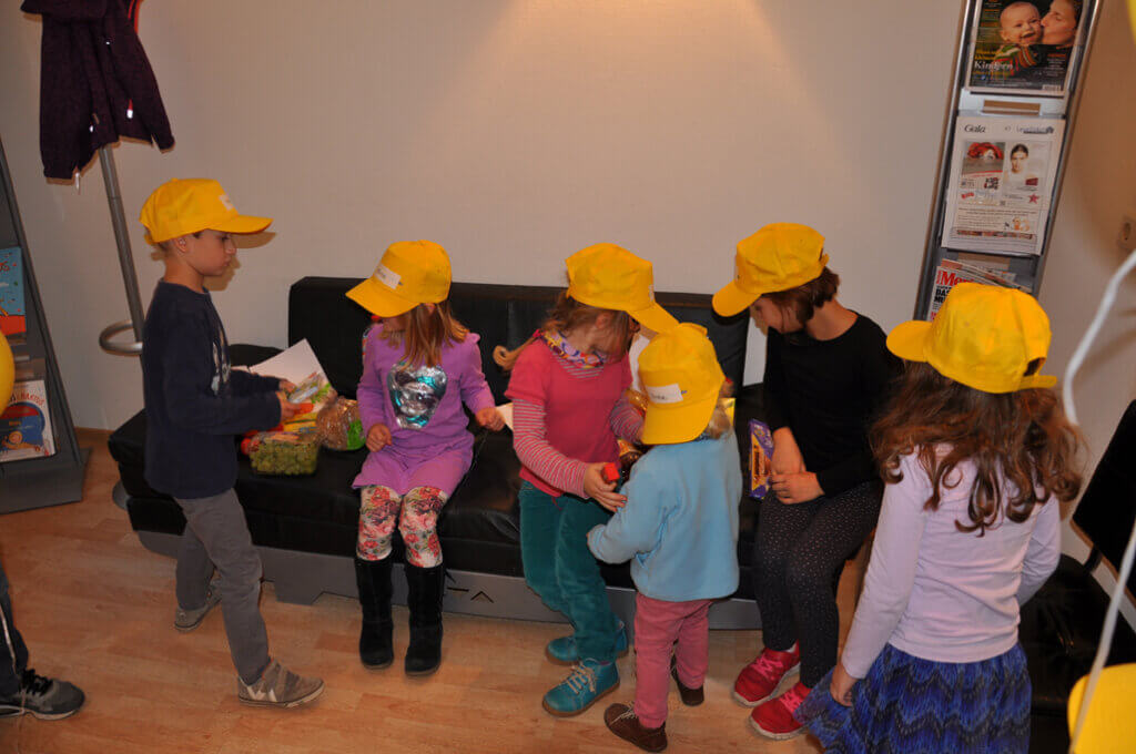 Kinder mit gelben Kappen sitzen gemeinsam im Wartebereich.