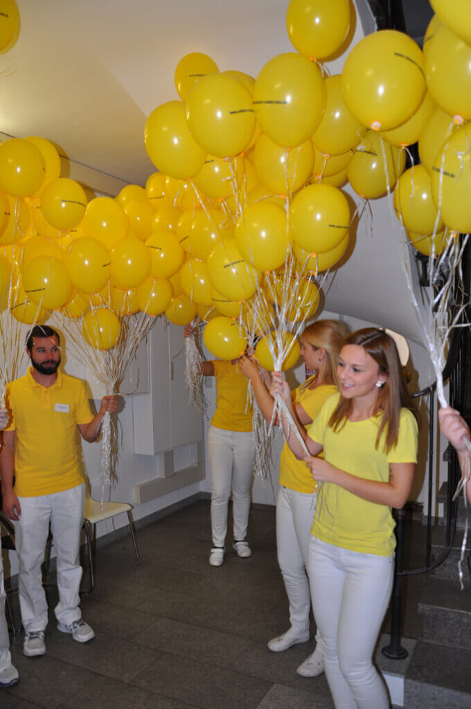 Mitarbeiterinnen und Mitarbeiter mit gelben Luftballons im Innenbereich.