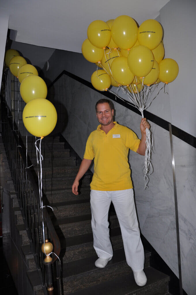 Mitarbeiter hält mehrere gelbe Luftballons auf einer Treppe.