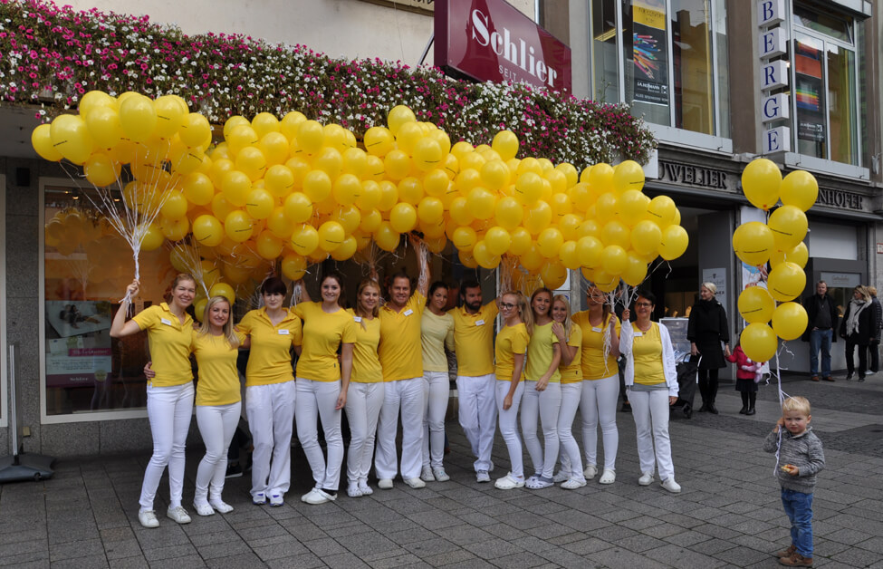 Praxisteam steht unter einer großen Menge gelber Luftballon und macht ein Gruppenfoto.