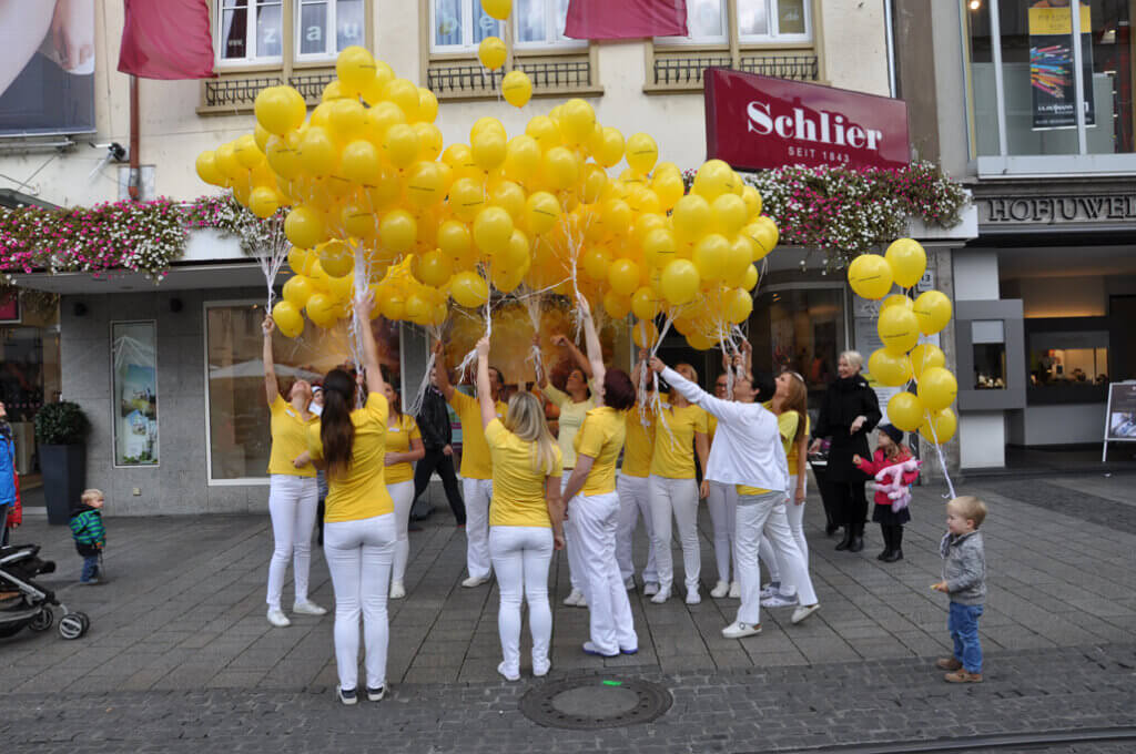 Praxisteam lässt gelbe Luftballons vor einem Gebäude fliegen.