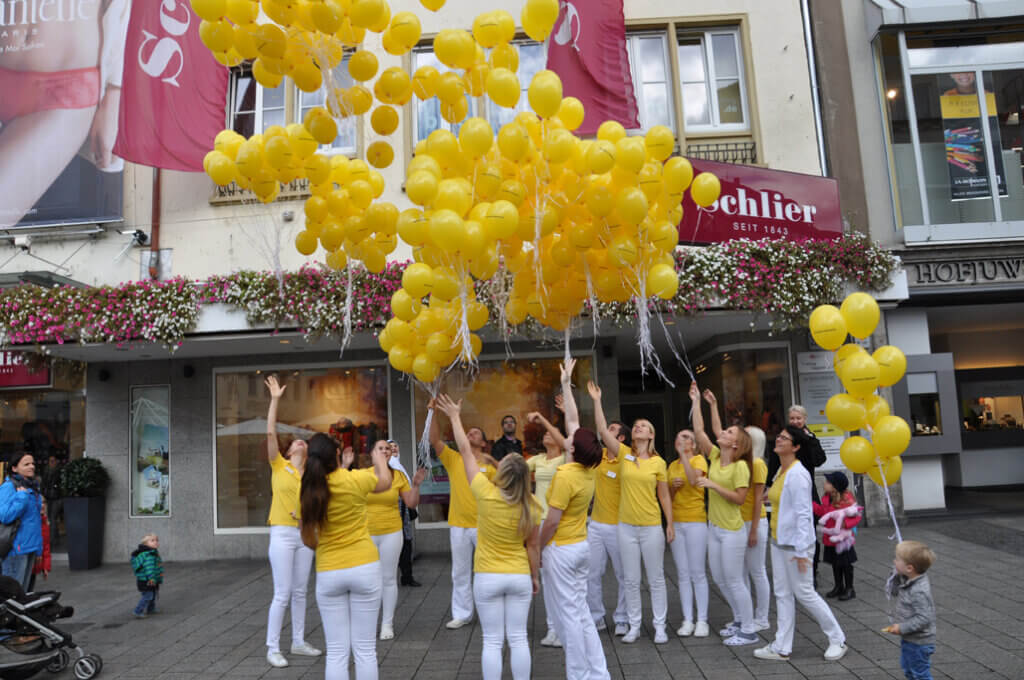 Praxisteam lässt gelbe Luftballons vor einem Gebäude fliegen.