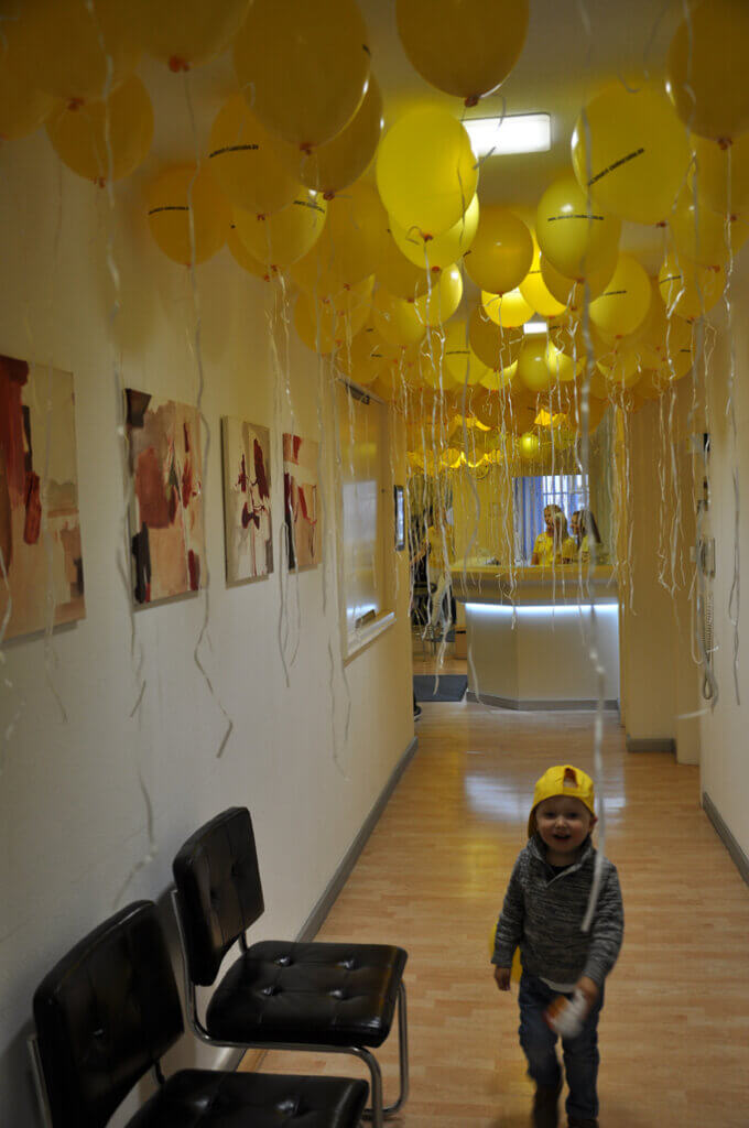 Flur der Zahnarztpraxis mit zahlreichen gelben Luftballons und einem glücklichen Kind.