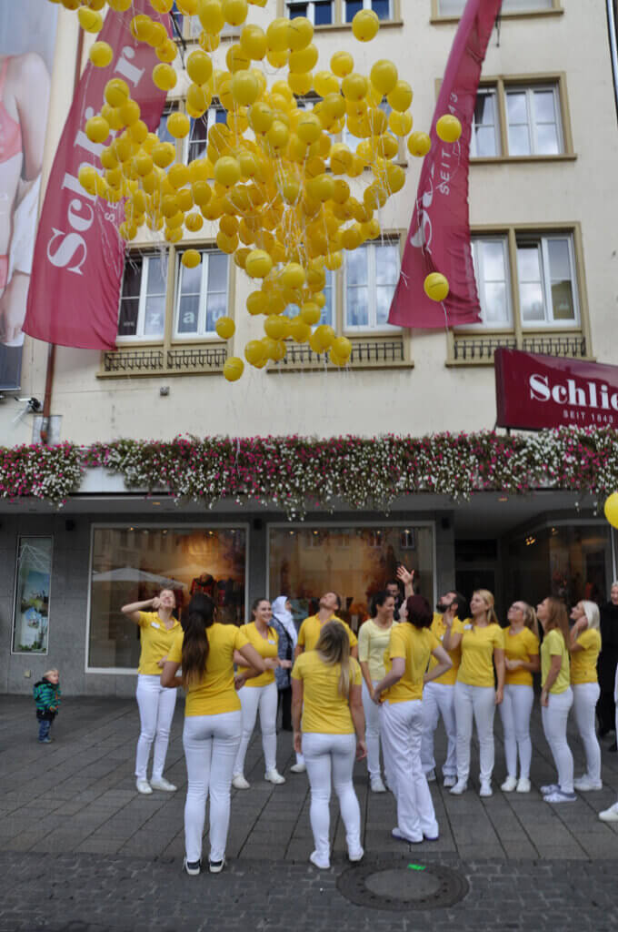 Praxisteam lässt gelbe Luftballons vor einem Gebäude fliegen.