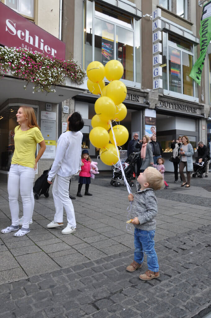 Kind mit vielen gelben Luftballons in der Hand.