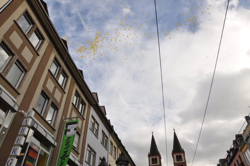 Gelbe Luftballons steigen über den Dächern der Stadt in den Himmel.